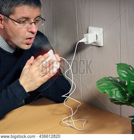 European Man Warms Hands From Portable Electrical Usb Heater, Connected To The Wall Outlet, Indoors 