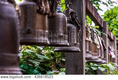 Many Metallic Bells Hanging In A Row On Wooden Pillars Outside In Thai Buddhist Temple. Lined With M