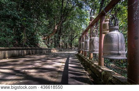 Many Metallic Bells Hanging In A Row On Wooden Pillars Outside In Thai Buddhist Temple. Lined With M