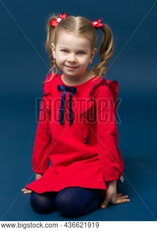 Charming Little Girl In Red Dress Sitting On Her Knees. Adorable Smiling Girl With Cute Two Ponytail