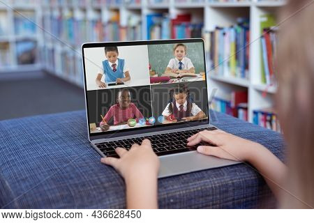 Caucasian girl using laptop for video call, with smiling diverse elementary school pupils on screen. communication technology and online education, digital composite image.