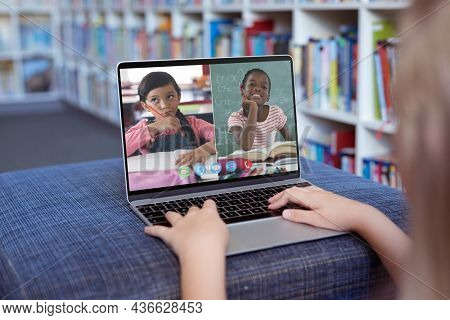 Caucasian girl using laptop for video call, with smiling diverse elementary school pupils on screen. communication technology and online education, digital composite image.