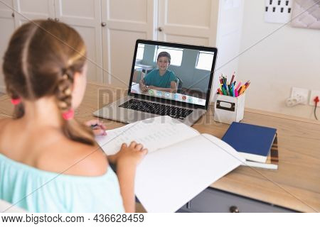Caucasian girl using laptop for video call, with smiling elementary school pupil on screen. communication technology and online education, digital composite image.