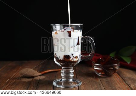 Pouring Milk Into Glass Cup With Delicious Grass Jelly At Wooden Table