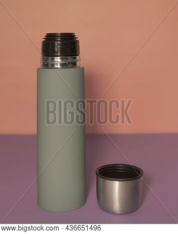Green Thermos With Open Lid On A Peach-fiolet Background