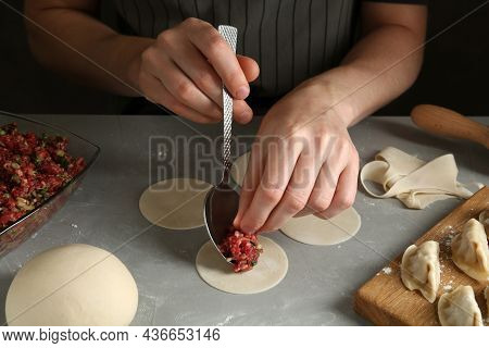 Woman Putting Gyoza Filling In Center Of Dough Wrapper At Grey Table, Closeup