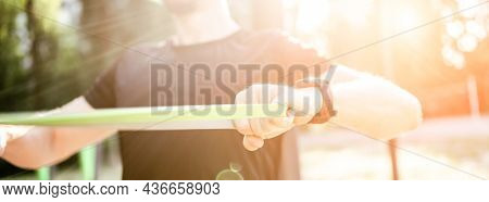 Strong man guy training with elastic rubber band at the stadium outdoors. Adult male person during workout for arms and chest with additional sport equipmant. Sportsman exercising outside