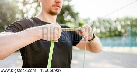 Sportive man guy training with elastic rubber band at the stadium outdoors with sunlight. Athlete male person during workout with additional sport equipmant