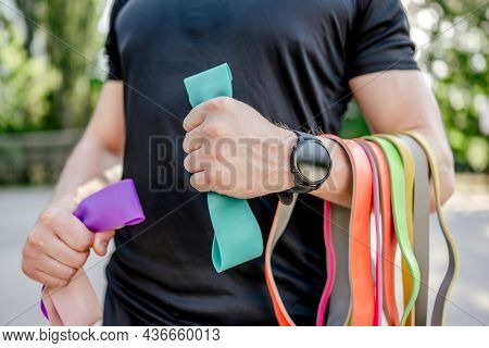 Strong man guy holding set of colorful elastic rubber bands at the stadium outdoors. Athlete male person during workout with additional sport equipmant