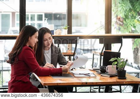 Young Businesswoman And Partnership Holding A Pen Pointing The Graph To Analyze The Marketing Plan W