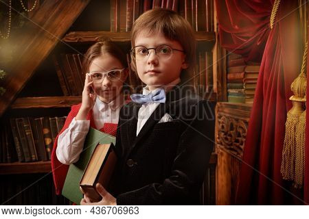 Pair of schoolchildren dressed in fashionable school clothes pose in a splended vintage interior by a bookcase with books in their hands. Kid's school fashion. 