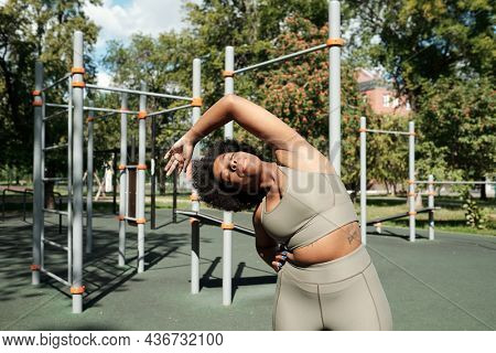 Young active plus size female doing side-bends on sunny morning on sportsground