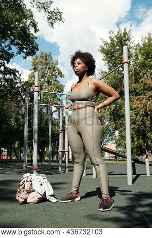 Young plus size woman in grey sportswear standing on sportsground in park in the morning