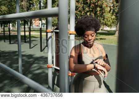 Young female in activewear looking at smartwatch on her wrist after training on sportsground