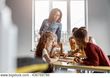 Happy Schoolchildren Using Geoboard In Classroom Together
