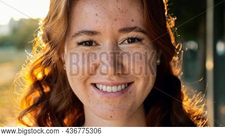 Portrait Of Pretty Young Woman With Curly Copper Flowing Hair And Freckles Smiling To Camera At Brig