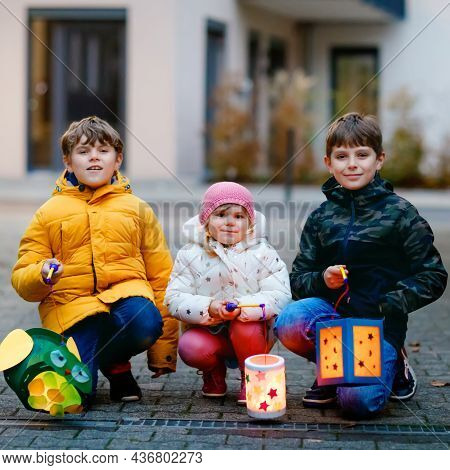 Little Toddler Girl And Two Kids Boys Holding Selfmade Lanterns With Candle For St. Martin Processio