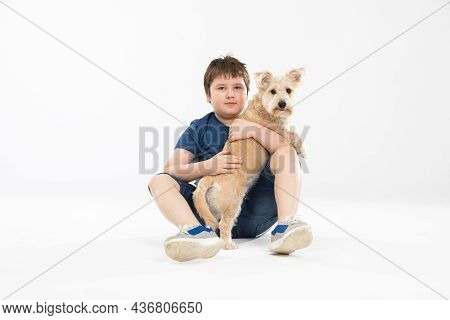 A Young Boy Sits On A White Background And In His Hands He Holds His Beloved Dog.