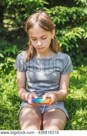 Preteen girl playing silicone antistress popit fidget toy outdoors, focus on fidget