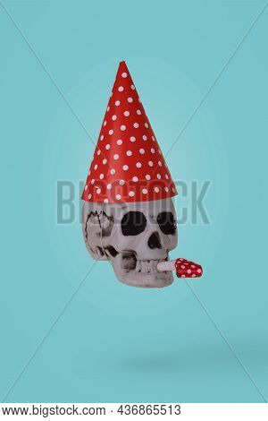 Human Skull  With A Red Birthday Cap And Whistle  Isolated On A Blue. Minimal Holiday Celebration Fu
