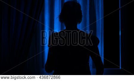 A Young Excited Woman In A Panic Runs Away From Her Pursuer Along A Dark Corridor. A Flickering Sign