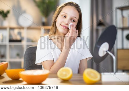 Pretty Female Teenger Sitting At Table While Cleaning Face With Cotton Pad And Looking At Mirror. Ha