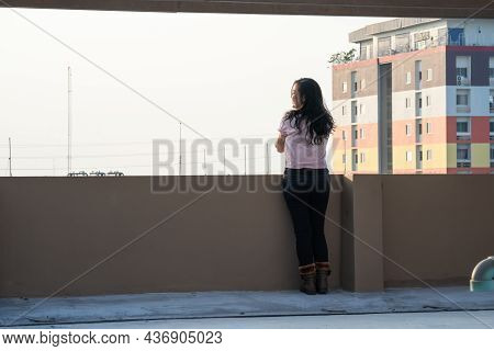 Asian Female Teen Stands Backside In Front Of City View At Rooftop Of The Building