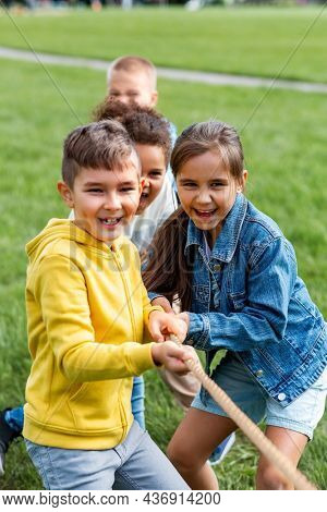 childhood, leisure and people concept - group of happy kids playing tug-of-war game and running at park