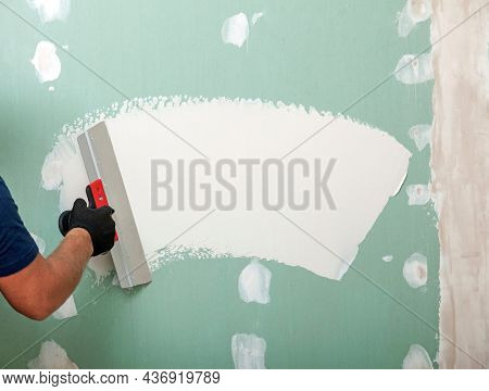 Hand with a spatula. Worker trowels putty on drywall with finishing putty