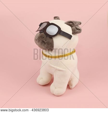 Plush Soft Light Beige Pug Dog Toy With Sun Glasses And Gold Collar Isolated On Pink Background. Sid