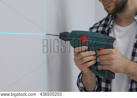 Man Using Cross Line Laser Level For Accurate Measurement And Drilling Hole In Light Wall, Closeup