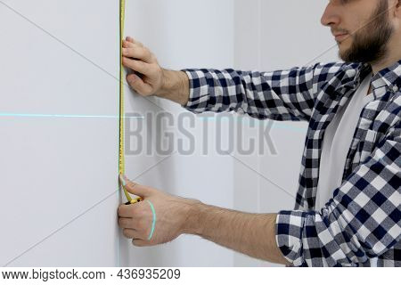 Man Using Cross Line Laser Level And Tape For Accurate Measurement On Light Wall, Closeup