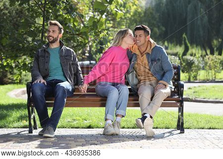 Woman Kissing Another Man While Holding Hands With Her Boyfriend On Bench In Park. Love Triangle