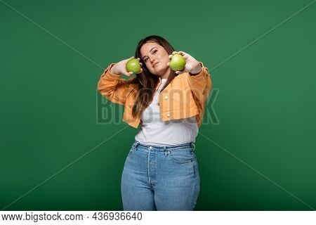 Young Woman With Overweigh Holding Apples And Looking At Camera Isolated On Green