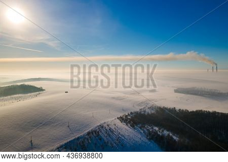 Aerial View Of Winter Landscape With Foggy Countryside And Distant Factory Pipes Emmiting Black Dirt
