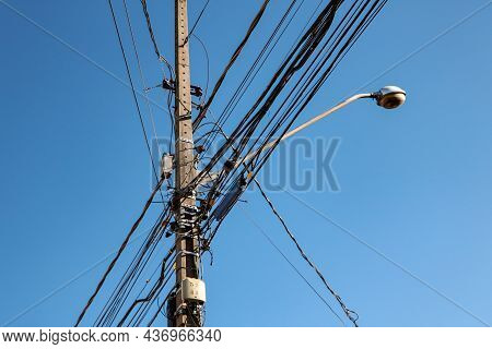 Public Lighting Electric Network Pole With A Tangle Of Wires, With The Lamp Rod And The Blue Sky In 