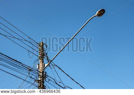 Public Lighting Electric Network Pole With A Tangle Of Wires, With The Lamp Rod And The Blue Sky In 