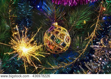 Christmas New Year Background. A Multi-colored Ball On A Christmas Tree And A Burning Sparkler. Chri