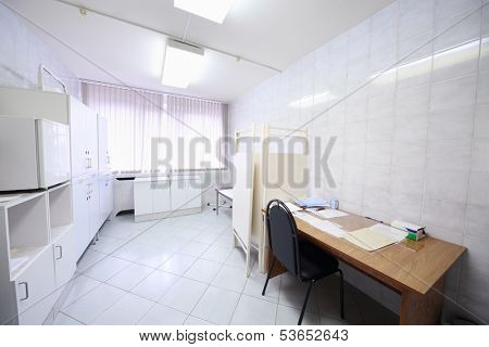 Interior of a light doctors consulting room with table, cabinet and folding screen