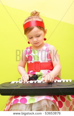 Mod little girl in a bright lush dress playing on a toy piano
