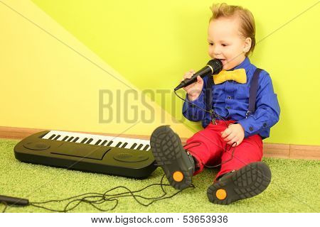 Boy in bright clothes sitting in the bright wall with a toy piano and singing into a microphone