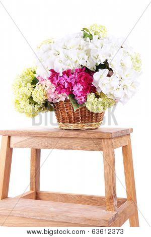 Wicker basket with flowers on small wooden ladder, isolated on white