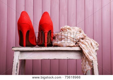 Red women shoes and scarf on bench on wooden background