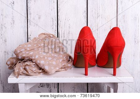 Red women shoes and scarf on bench on wooden background