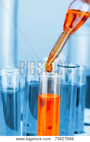 Laboratory pipette with drop of color liquid over glass test tubes, close up