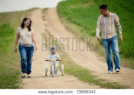 Family with little boy on tricycle in nature