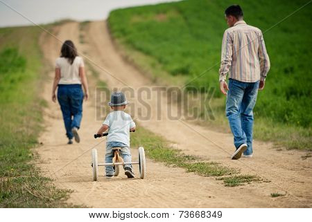 Family with little boy on tricycle in nature