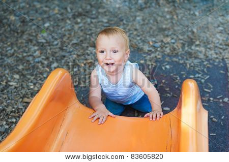 Adorable toddler boy having fun outdoors, climbing on playground