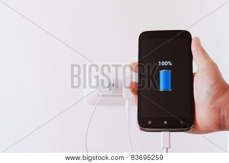Female Hand Plugging In The Plug Of Her Smartphone In A Socket