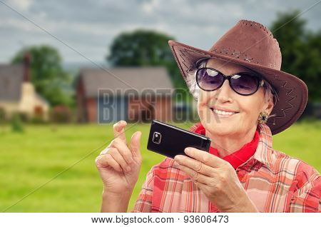 Old cowgirl surfing internet on smartphone in ranch